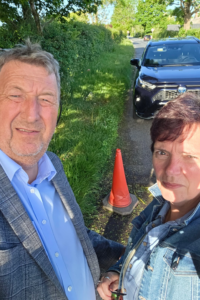 PaveVent™ founders Steve and Sarah Bays standing by their car, looking frustrated at a severe road pothole marked by a traffic cone.